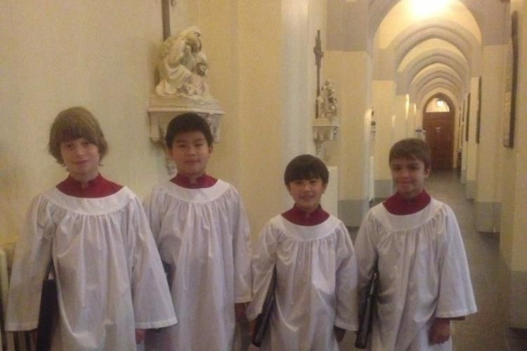 Four choristers in service robes standing informally in Cathedral aisle smiling at camera