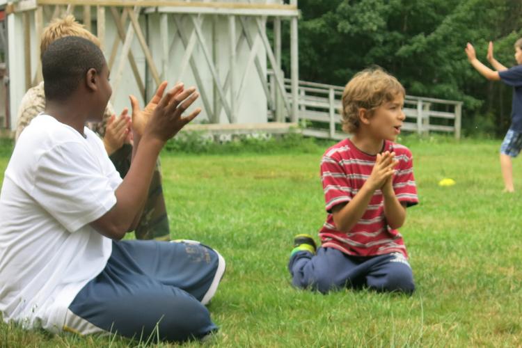 Boy choristers sitting on grass at choir camp, clapping hands