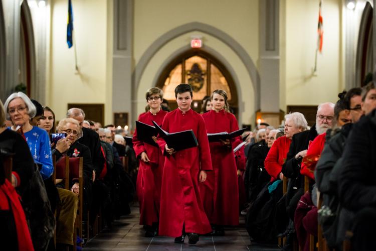 Boy choristers processing down centre aisle during performance, with large audience on either side