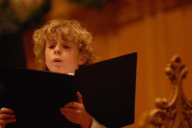 Young chorister singing and looking at music in black music folder