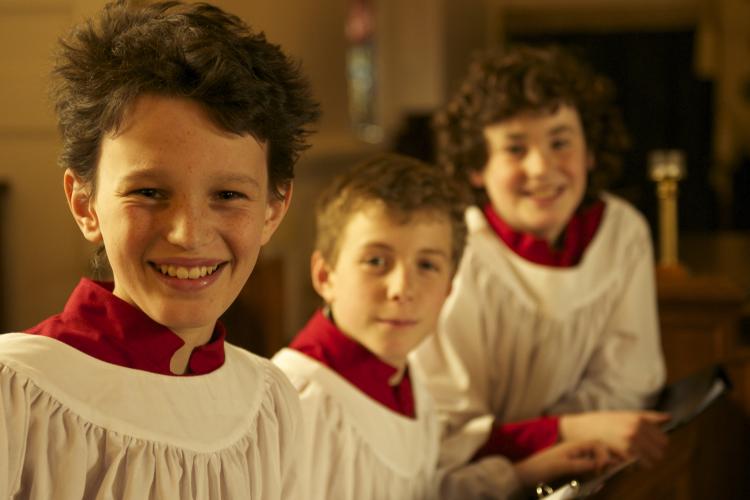 Three boy choristers in choir stall, with service robes on, smiling at the camera