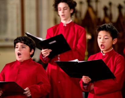 Three choristers in red robes singing during performance