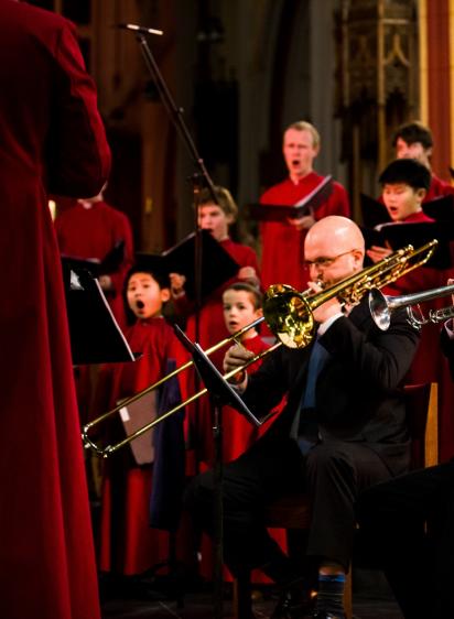 Choir in red robes singing with trombone player in foreground
